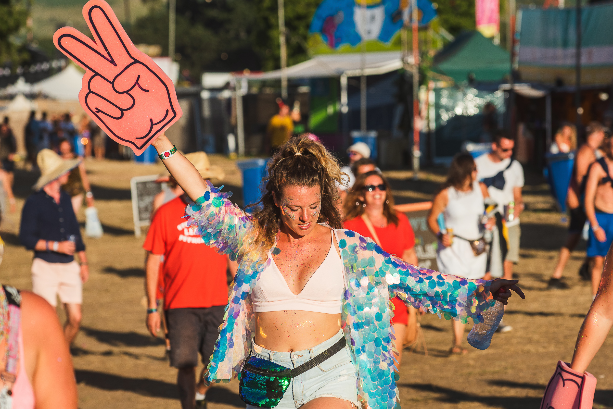 Young girls takes a stroll around the Bestival site with a large red foam hand with the two fingered peace gesture