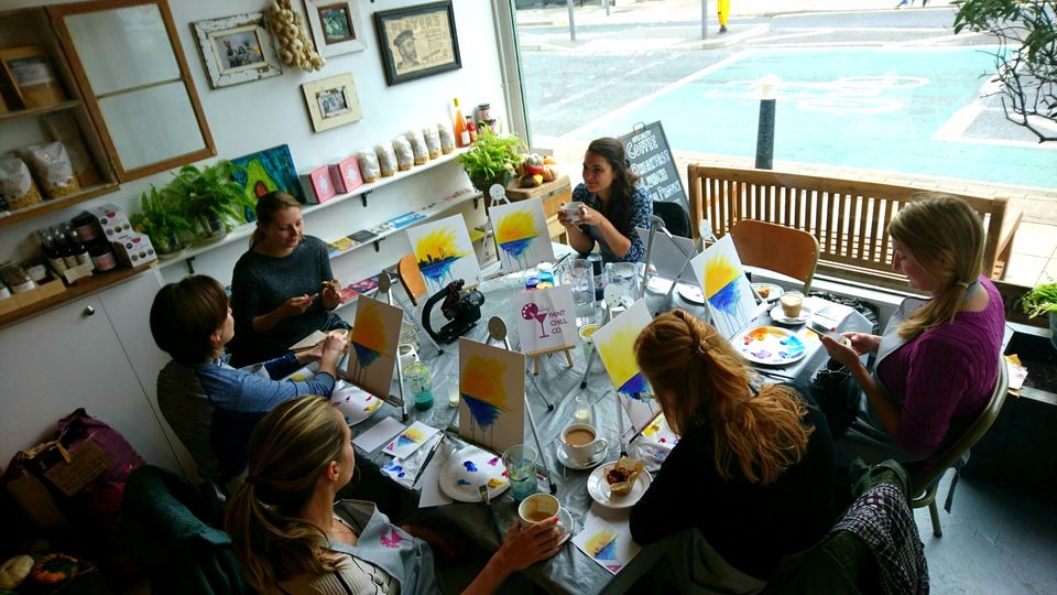 A group of people painting around a table at a Coffee Morning Paint event