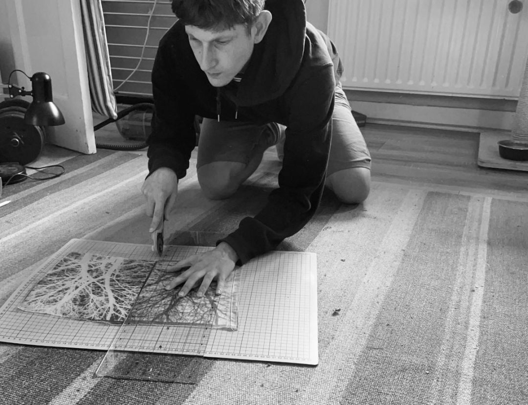 A male artist kneeling on the floor over his artwork. The photo is black and white.